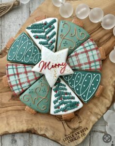 Collection of christmas tree cookies with royal icing details. One star sugar cookie on the top states "Merry" in red frosting.