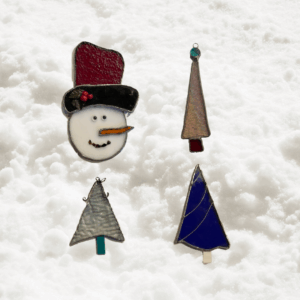 Stained glass Christmas ornaments shaped like trees and a snowman displayed on fresh white Colorado snow