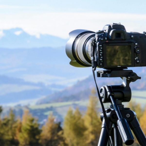 DSLR camera mounted on a tripod capturing a landscape scene with trees in the foreground and distant Colorado mountains in soft focus